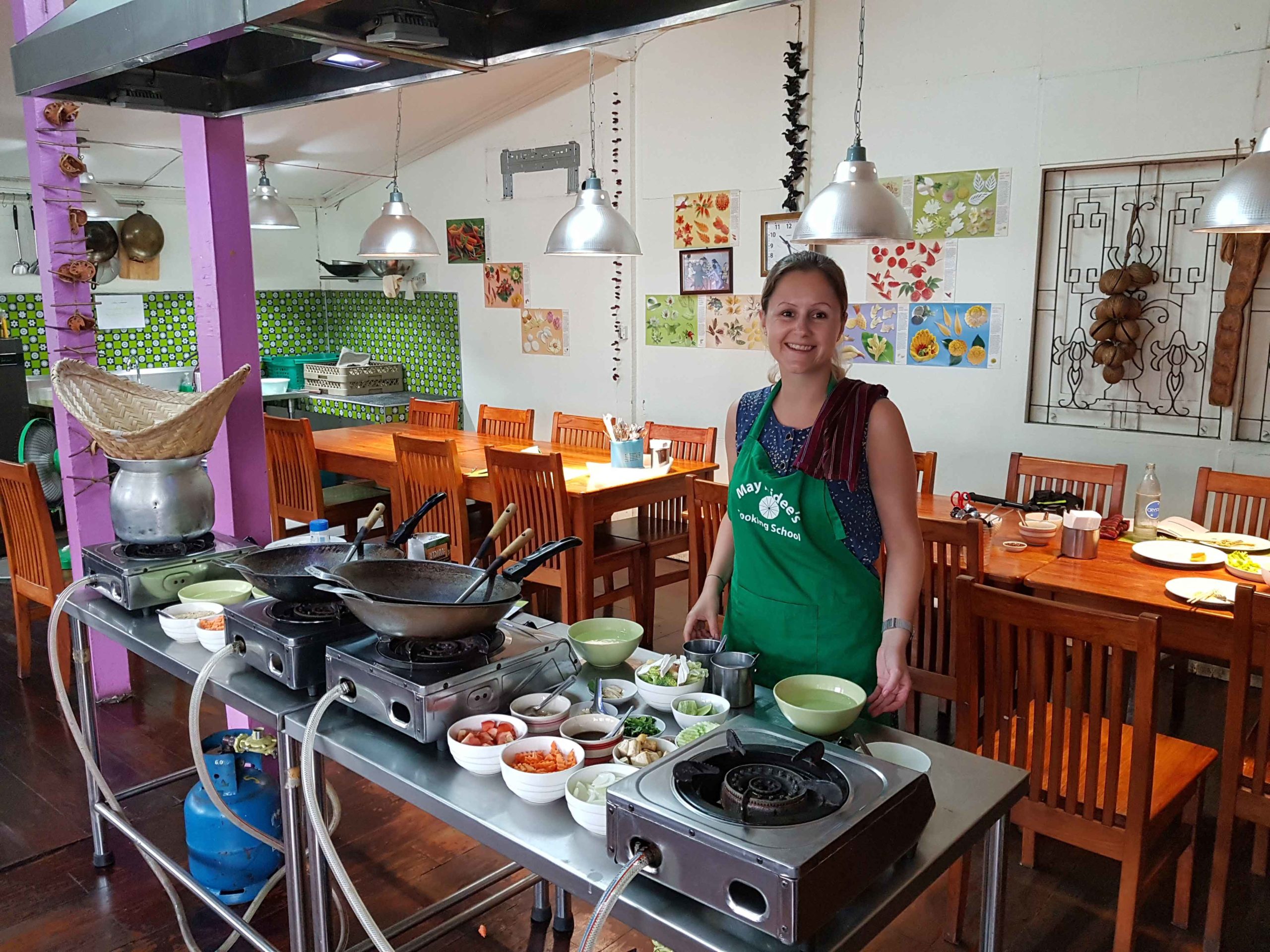 Silvia mit Kochschürze vor dem Wok und den Zutaten in der Küche von May Kaidee's Cooking School in Bangkok, Thailand