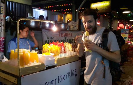 Mann isst frisch aufgeschnittene Mango am Street Food Stand am Nachtmarkt von Chiang Mai, Thailand