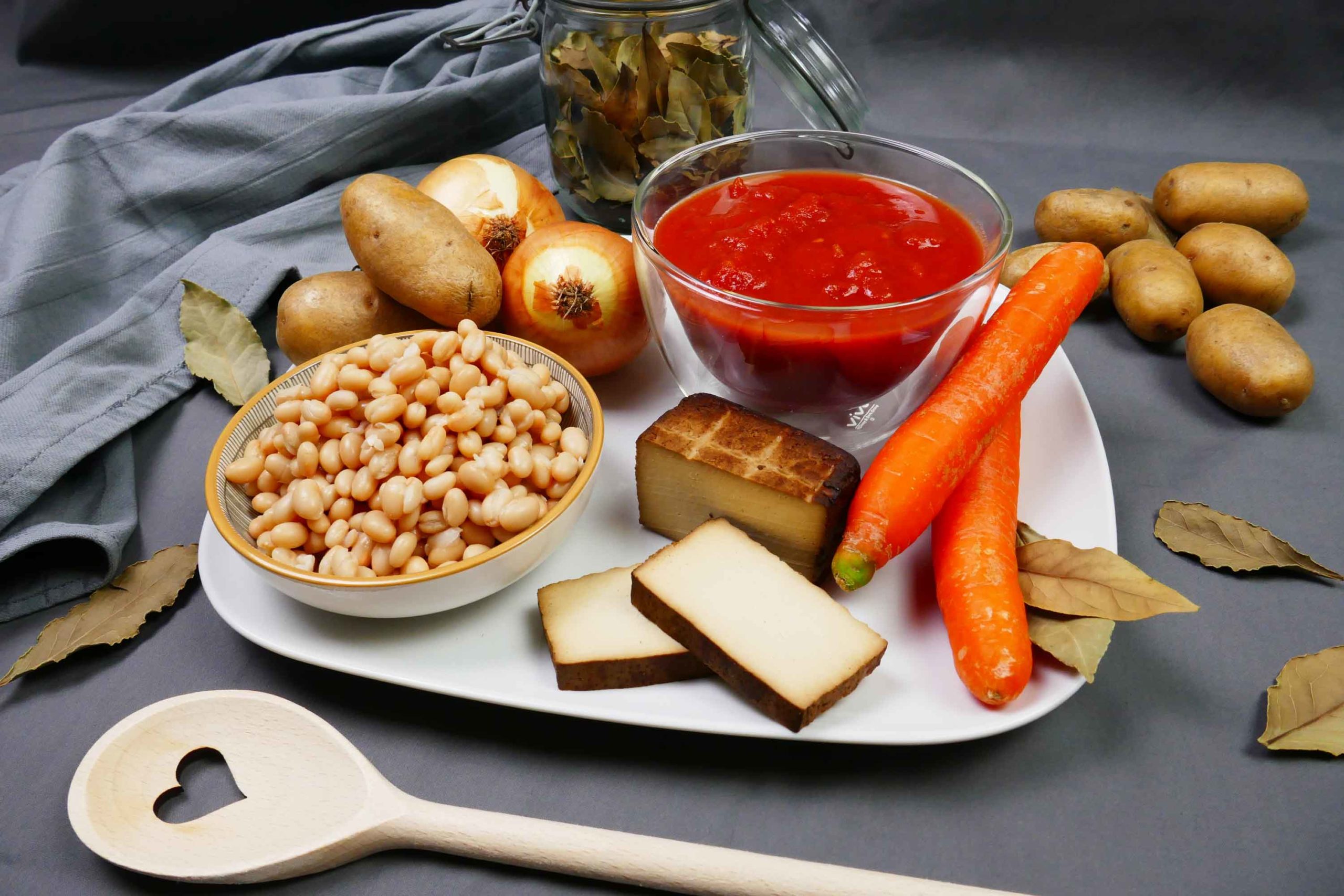 Serbische Bohnensuppe Zutaten, weiße Bohnen, geräucherter Tofu, Karotten, Tomatenpassata, Kartoffeln, Lorbeerblätter, Kochlöffel