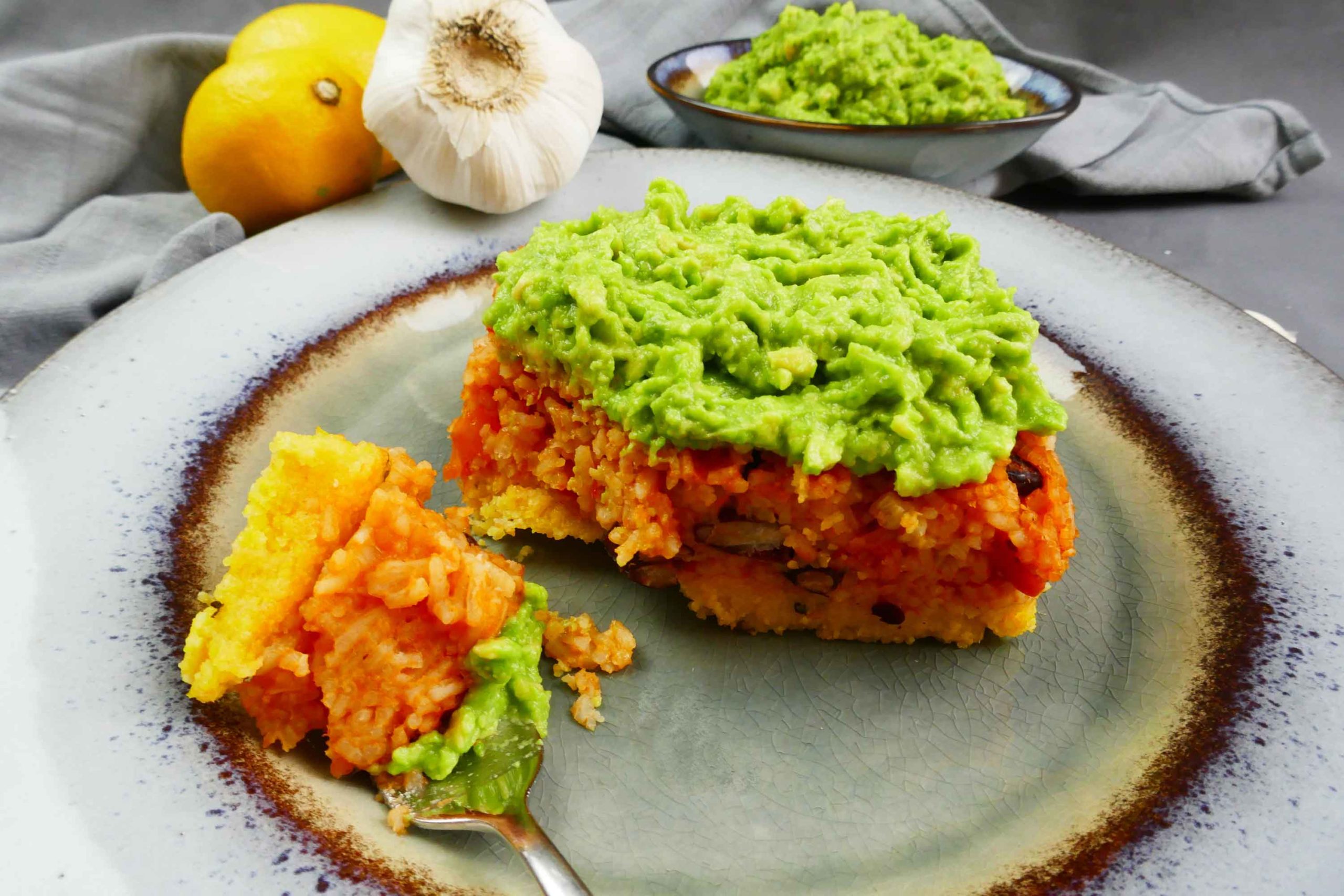 Polentaschnitte mit Reis und Bohnen und frischer Avocado als Topping auf einem Teller angerichtet